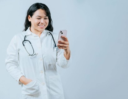 Female healthcare worker holding cellphone. Smiling asian doctor using smartphone isolated, Young