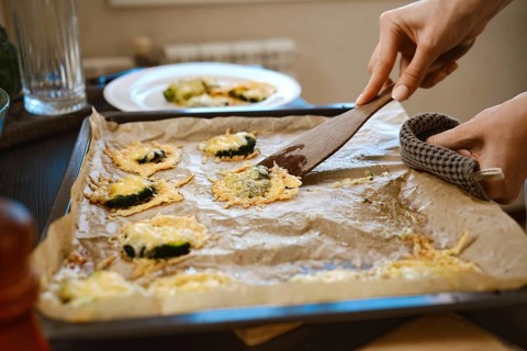 Unrecognizable woman transfers roasted smashed broccoli with cheese from baking sheet to plate