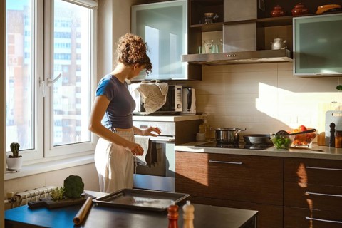 Woman turns on oven to preheat. The sunlight comes through the window. Various ingredients are on