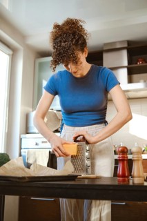 Woman grates cheese in a bright kitchen while preparing smashed broccoli. The scene shows cooking