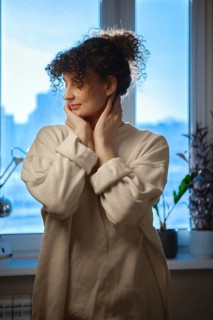 Young woman looks out the window while touching her face in a cozy indoor setting during daytime