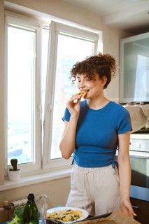 Woman bites smashed broccoli with cheese. The window opens to a city view. Fresh ingredients are on
