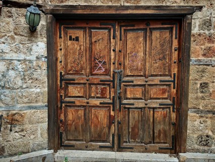 Old wooden door with graffiti on a stone wall, next to it an old lamp, Antalya Turkey