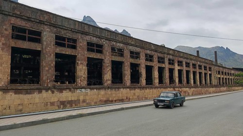 Abandoned large building and a car on a quiet road in the background mountains and clouds,