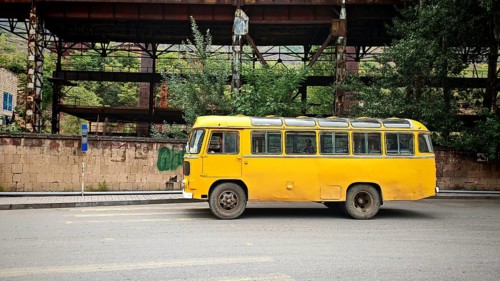 An old yellow bus is parked in front of an abandoned industrial plant in an urban area, Alaverdi,