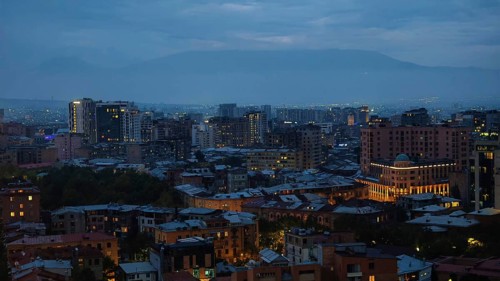 Nighttime city scene at dusk with illuminated buildings and mountains in the background, Yerevan,