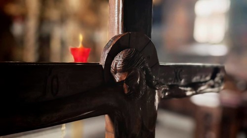 Detail of a wooden cross with a burning candle in the background in an atmospheric light, North