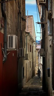 Narrow, shady alley with old buildings and visible air conditioners, Koper, Slovenia