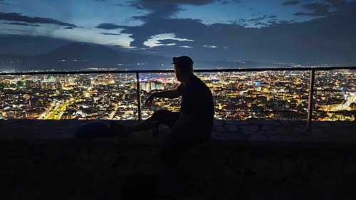 Person in front of illuminated cityscape at night, relaxed atmosphere, Prizren, Kosovo