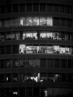 Black and white photo of an illuminated office building with visible floors and people, Tirana,