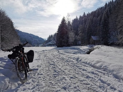 Snowy landscape with bike and hut surrounded by forest under the winter sun
