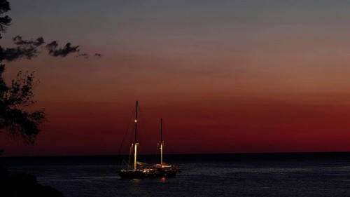 Sailing boat on still sea at sunset, illuminated by dwindling daylight
