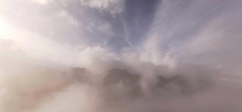 Soft cloud formations over foggy mountain peaks in mild light