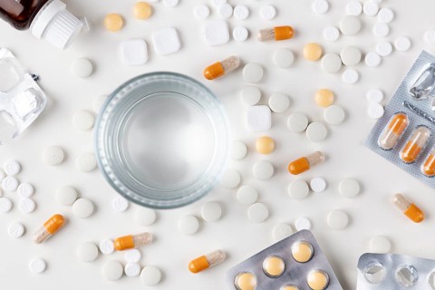 Table with scattered tablets, blister packs and a glass of water