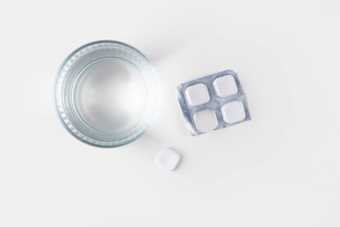 Glass of water with packaging and tablets on a white surface