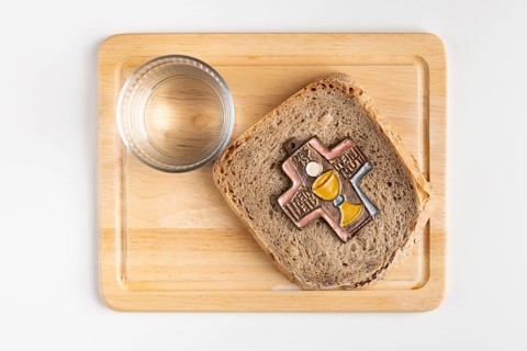 Bread with cross symbol on a wooden board with a glass of water next to it, white background