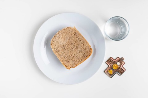 Slice of bread on a plate with a water glass and a cross symbol on a plain white background,