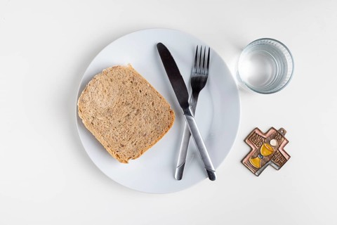 A plate with a slice of bread, cutlery, water glass and cross, Lent