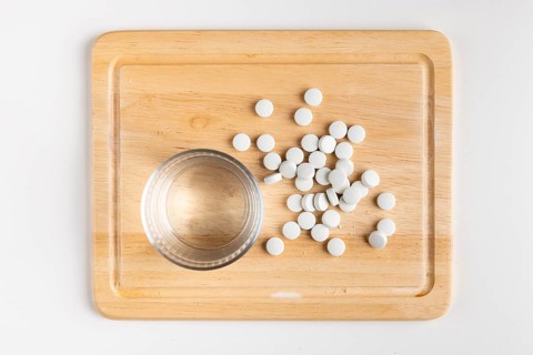 Wooden board with glass of water and scattered tablets