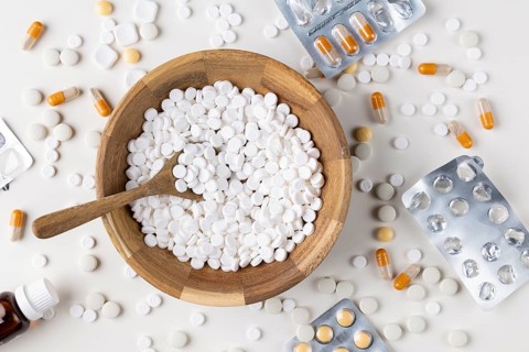 Wooden bowl full of tablets with a spoon and scattered blister packs