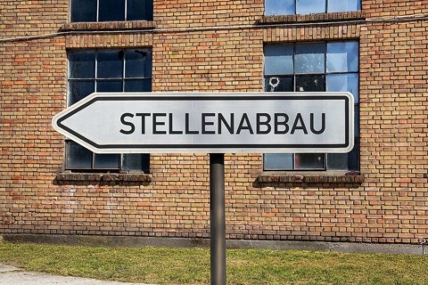 (photo montage) Directional arrows with the inscription JOB REDUCTION in front of an old industrial