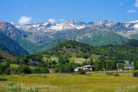 Picturesque mountain landscape with snowy peaks, green hills and meadows under blue skies,