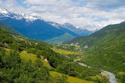 Extensive mountain landscape with river in the valley and lush green forests under blue sky,