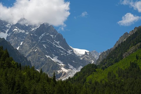 Mountain landscape with snow-capped peaks and a forest, partly covered by clouds, Chalaadi
