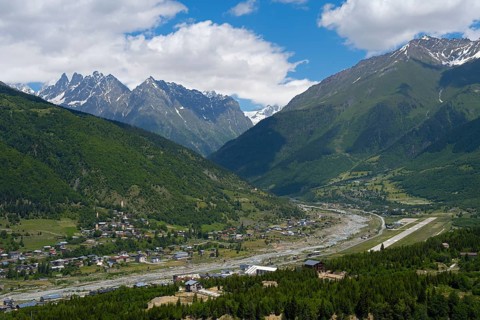 A view of a valley with a river surrounded by mountains and a village in the foreground, right
