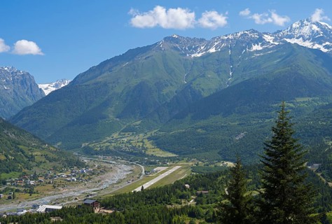 Valley with river and adjacent mountains under a bright blue sky, in the middle an airport, Mestia,