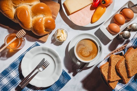 Breakfast with toast, stollen, honey, cheese, ham, coffee, butter, peppers and eggs on a table