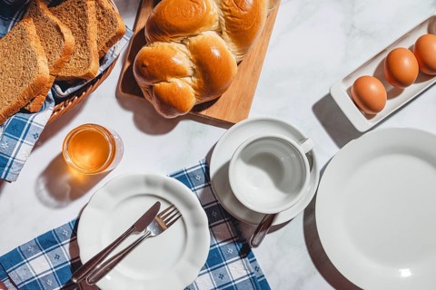 Breakfast items such as toast, stollen, eggs and honey on a white table