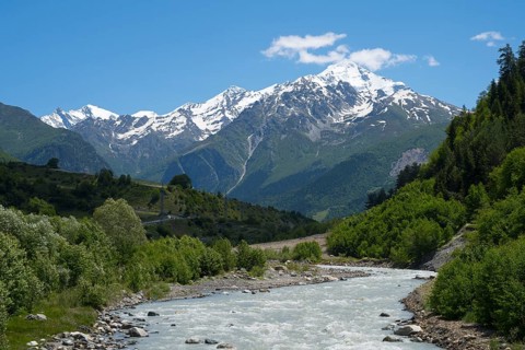 Fast-flowing river in a wooded valley against a backdrop of snow-capped mountains, Mulkhra River