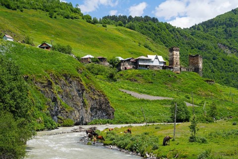 Idyllic landscape with river and village on a hill, horses grazing in the foreground, Davberi on