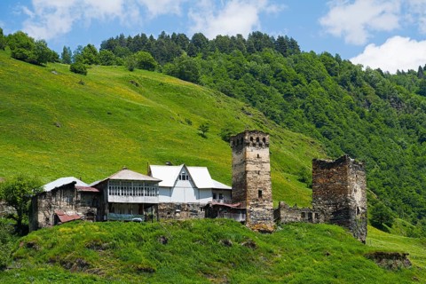 Medieval village with tower on a hill in the background, surrounded by green landscape and clear