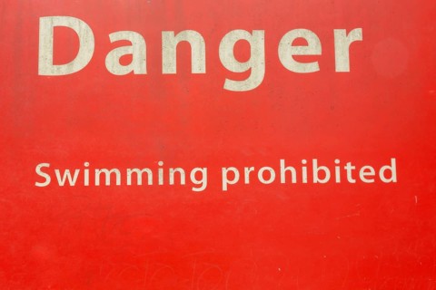 Danger Swimming Prohibited in white letters on red painted metal public notice sign in public park,