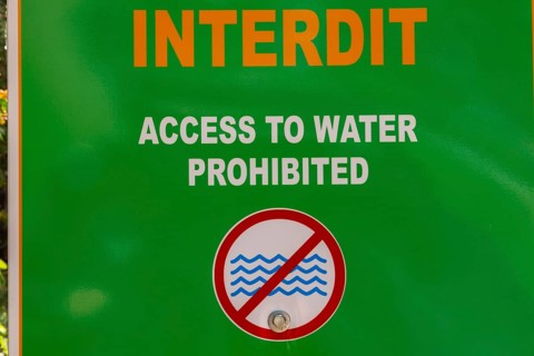 Posted bilingual French and English language warning Access to Water Prohibited in white and orange