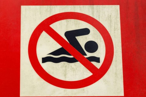 Close-up of posted painted red and white with illustrated swimmer in solid black on metal pictogram