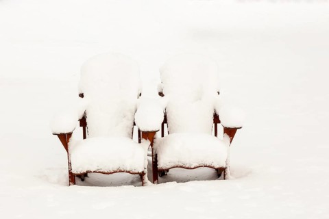 Two brown stained wooden Adirondack chairs covered in freshly fallen winter like snow in public