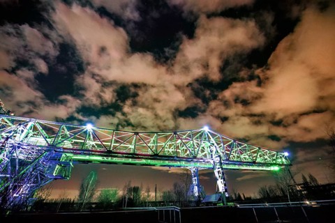 Illuminated bridge at night under a dramatically cloudy sky with green light, Landschaftspark