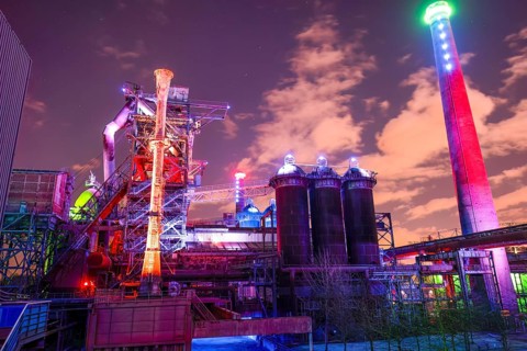 Colourful lighting on industrial buildings with visible chimney, Landschaftspark Duisburg Nord,