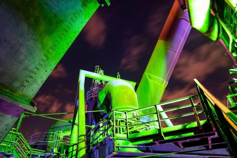 Detailed view of a metallic industrial plant illuminated with green and purple lights,