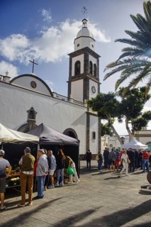 Church front with market scene, people gather around tents on a sunny square, Arrecife Lanzarote