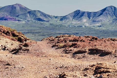 Volcanic mountain landscape with red earth formations and distant mountains, Playa Blanca Lanzarote