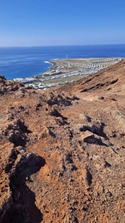 View from a rocky volcanic mountain (Montana Roja) to the distance and the blue sea, Playa Blanca