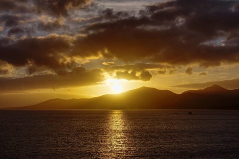 Sunset over the sea with golden reflections on the water surface, mountains on the horizon, Puerto