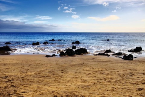 Peaceful sandy beach with rocks and calm sea under a wide sky, Puerto del Carmen Lanzarote