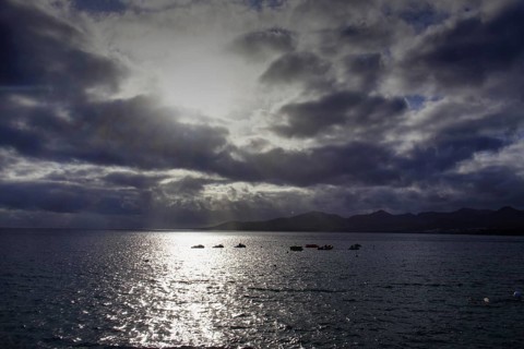 Dramatic atmosphere over the sea, clouds obscuring the sun, reflecting light on the water, Puerto