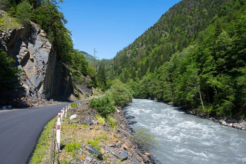 Mountain road next to a flowing river in a green, wooded landscape in clear summer weather, Enguri