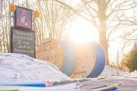 Sun rays fall on cable rolls next to a construction site sign surrounded by snow, fibreglass